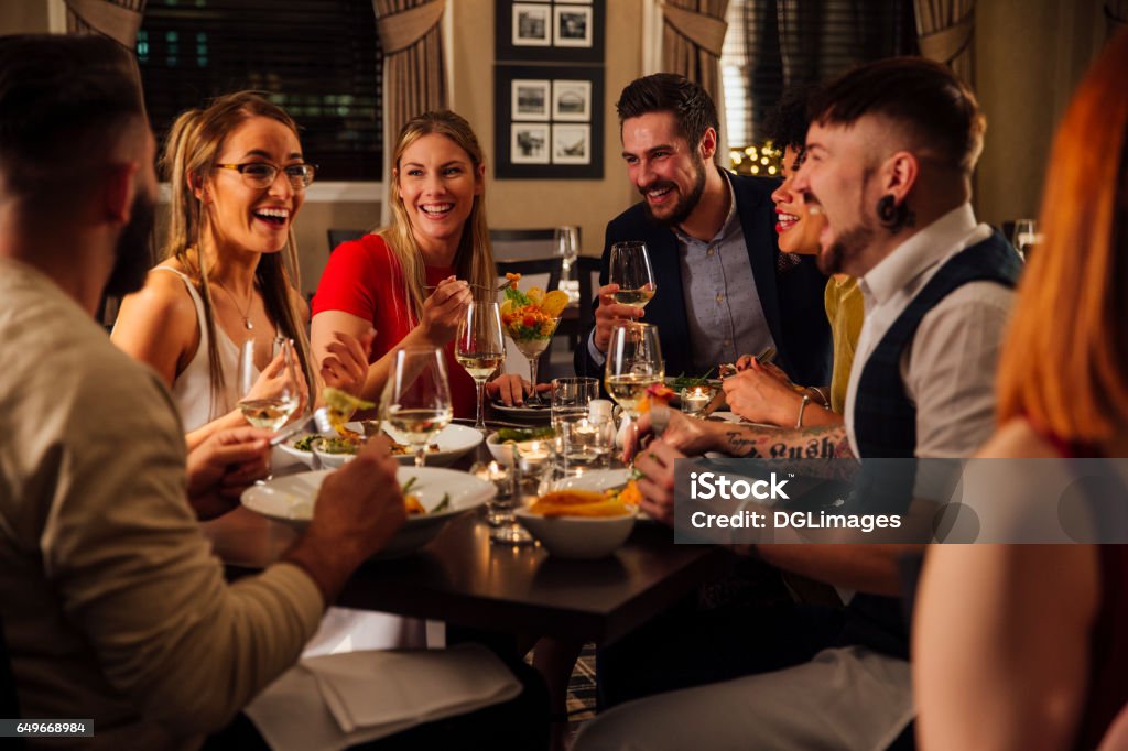 Friends Enjoying A Meal Group of friends are enjoying a meal together. They are talking and laughing while eating their starters and drinking champagne. Dinner Stock Photo