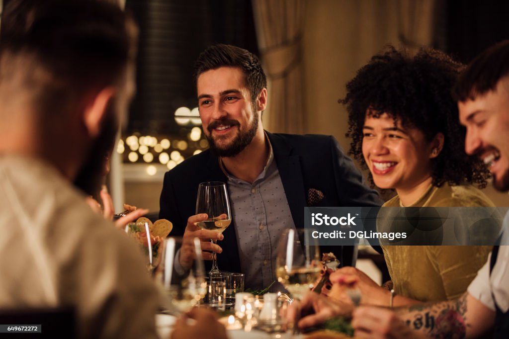 Socialising Over A Meal Group of friends are enjoying a meal in a restaurant. They are are talking and laughing while eating and drinking wine. Dinner Stock Photo