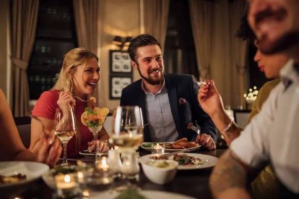 Mid adult couple are socialising over a meal in a restaurant. They are eating starters and drinking champagne while laughing and talking.