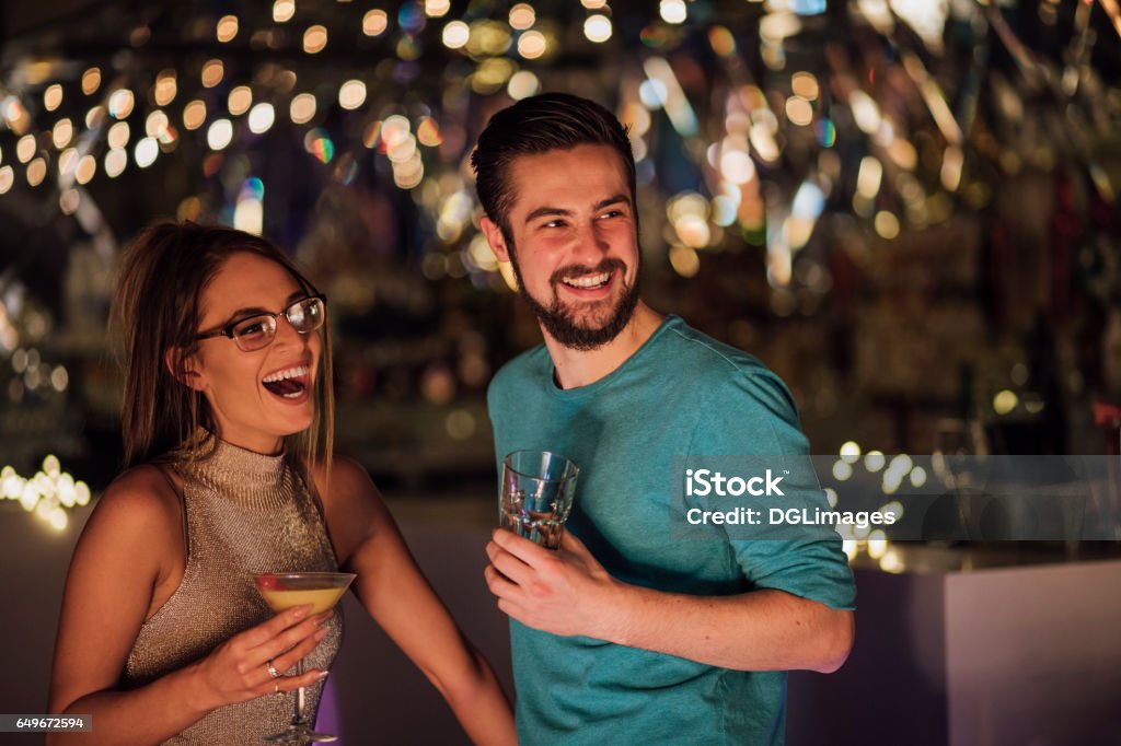 Couple In A Nightclub Young adult couple are socialising in a nightclub with cocktails. Theya re laughing and looking at someone out of the frame. Bar - Drink Establishment Stock Photo