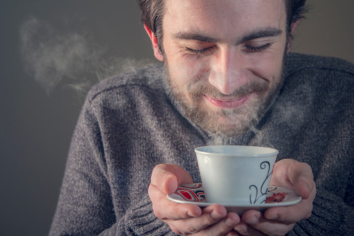 Young man enjoying the smell of his hot beverage, tea or coffee, anticipating the sweet taste