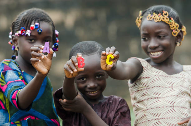 Learning the Alphabet - Beautiful African Portrait of Children Smiling Outdoors African children holding small colored letters in front of camera poverty child ethnic indigenous culture stock pictures, royalty-free photos & images