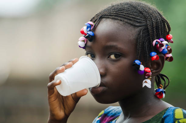 Water for Africa - African Girl Drinking Young african girl with traditional accessories in hair drinking and looking at camera poverty child ethnic indigenous culture stock pictures, royalty-free photos & images