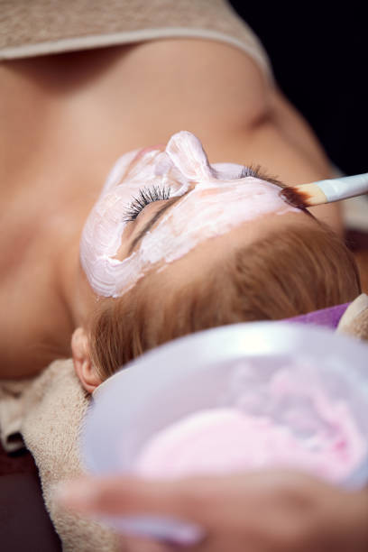 Girl receiving cosmetic pink facial mask Young beautiful girl receiving pink facial mask in spa beauty salon women facial mask mud cucumber stock pictures, royalty-free photos & images