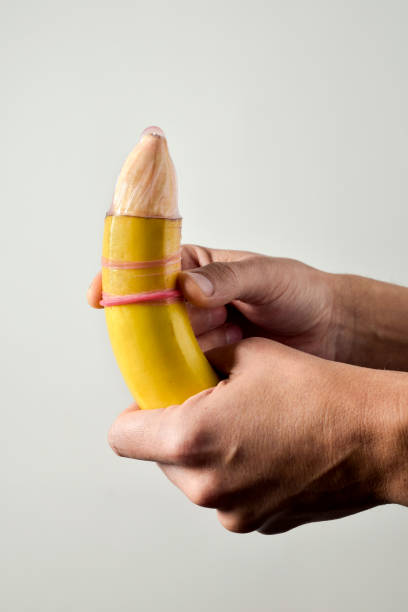 homme déballant un condom au-dessus d’une banane - condom sex education contraceptive aids photos et images de collection