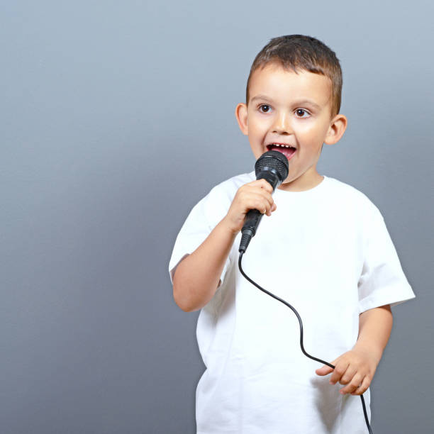 istock Cute little boy kid singing on microphone against gray background 649722040