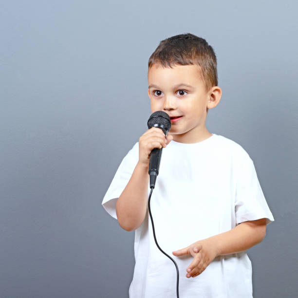 istock Cute little boy kid singing on microphone against gray background 649722044