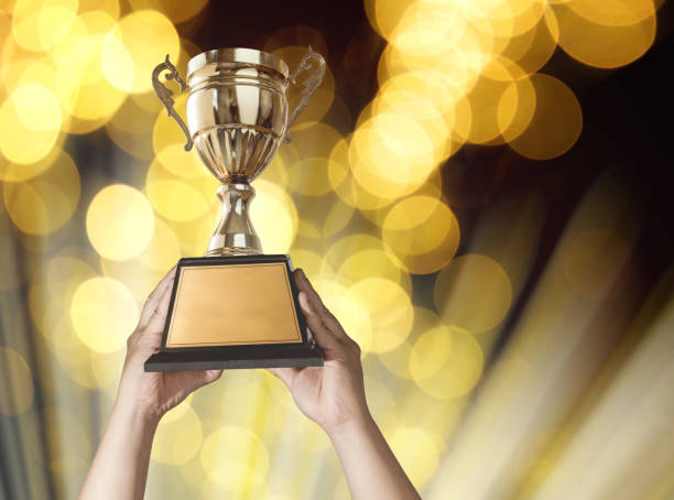 istock a man holding up a gold trophy cup with bastract gold light bokeh background copy space ready for your trophy design. 649741704