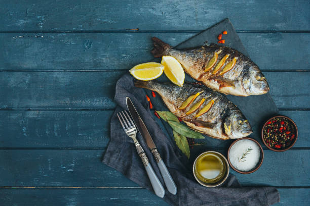 fish meat on a black tray with herbs and spices on top of a rustic wooden table - prepared fish seafood barbecue grilled imagens e fotografias de stock