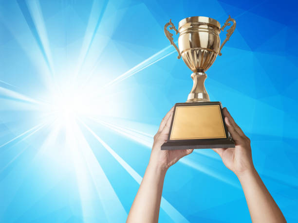 istock a man holding up a gold trophy cup with abstract blue light and modern background copy space ready for your trophy design. 649757126