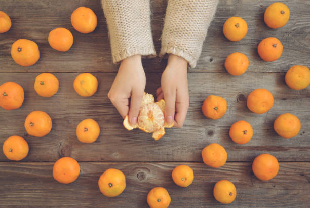 plano pone vista de manos de mujer pelar mandarinas frescas en la mesa de madera - concepto de otoño - mano sobre cadera fotografías e imágenes de stock