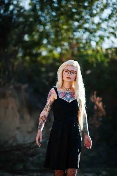 Photo of Young tattoo blonde girl on black dress and glasses posed background of career