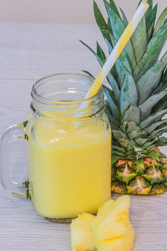 Pineapple smoothie in jar with pineapple fruit near. Yellow and white straw.