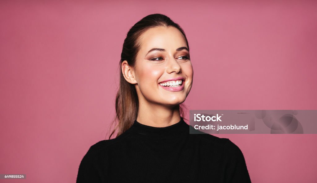 Beautiful female model standing and smiling Portrait of caucasian female model standing and smiling against pink background. Beautiful woman with perfect skin and makeup looking away. Smiling Stock Photo