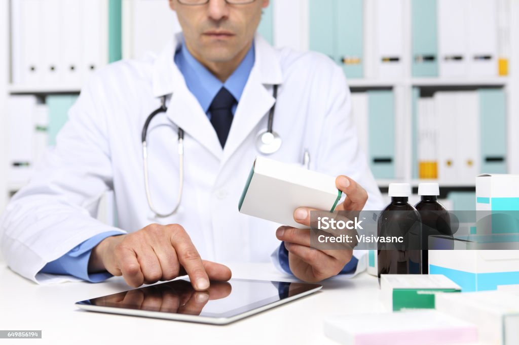 Doctor reading a Digital Tablet with drug boxes in hand  at Office Desktop. Health care, Medical and Pharmacy Concept. Prescription Medicine Stock Photo