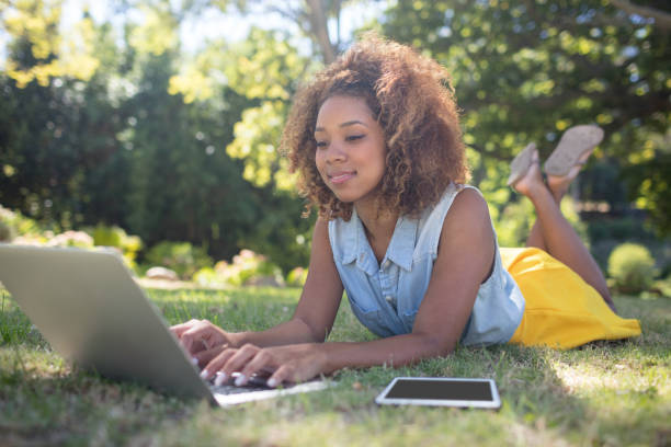 istock Smiling woman lying on grass and using laptop 649856710