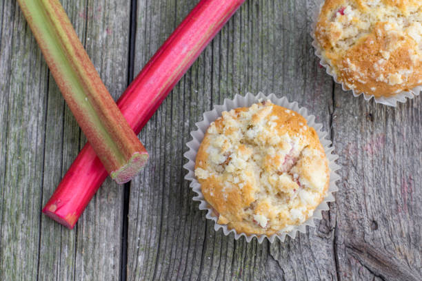 Top View on Rhubarb muffin in paper cups with rhubarb petioles in the background stock photo