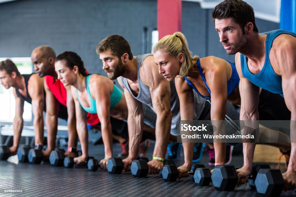 People doing push-ups with dumbbell in gym People doing push-ups with dumbbell while exercising in gym 20-29 Years Stock Photo
