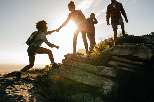 Young people on mountain hike at sunset Group of hikers on a mountain. Woman helping her friend to climb a rock. Young people on mountain hike at sunset. mountain climbing photos stock pictures, royalty-free photos & images