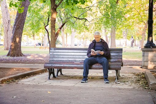 Senior man reading book alone in public park