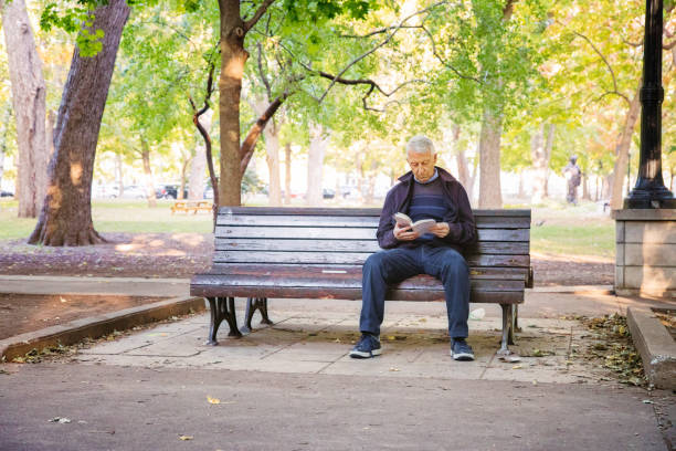 starszy mężczyzna czyta książkę sam w publicznym parku - men reading outdoors book zdjęcia i obrazy z banku zdjęć