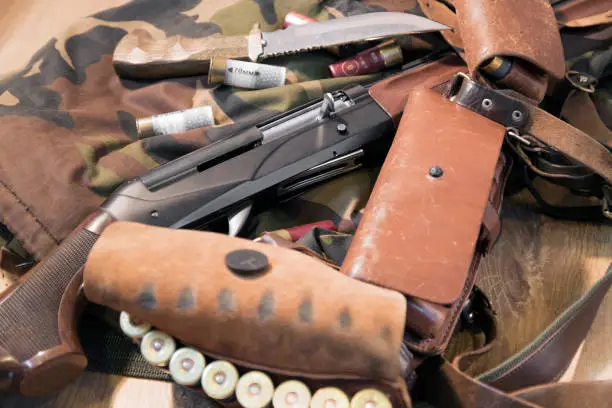 Semi-automated shotgun, wood trim, big hunting knife, brown bandolier and white and red cartridges, camouflage background