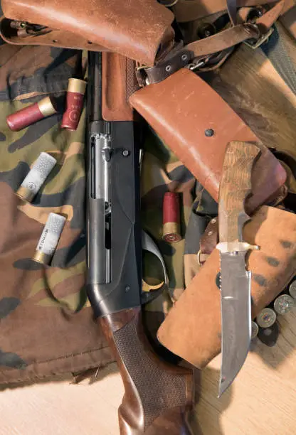 Semi-automated shotgun, wood trim, big hunting knife, bandolier and white and red cartridges, camouflage background