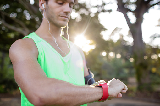 Man listening to music and checking time while jogging in park on a sunny day