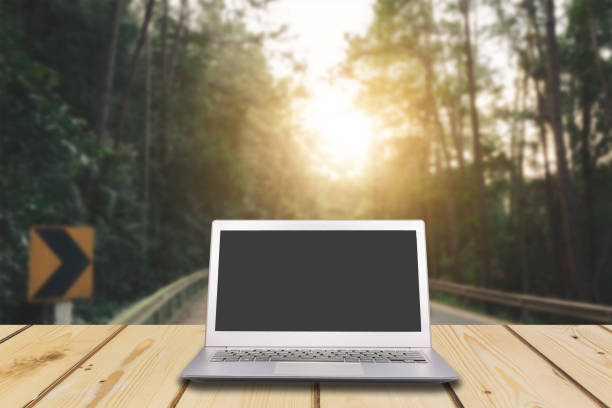 istock Laptop with blank screen on wooden table with dark misty forest, road and flare light background, can used for display or montage your products 649946236