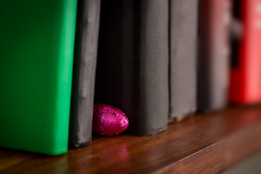 Foil wrapped easter chocolate hidden on wooden book shelf