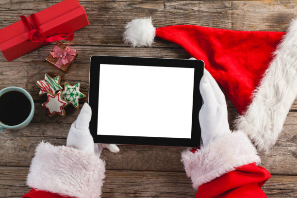 istock Santa claus using digital tablet on wooden plank 649987296