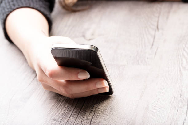 Female hand resting on a rustic grey wooden table holding a modern mobile phone as though reading or texting