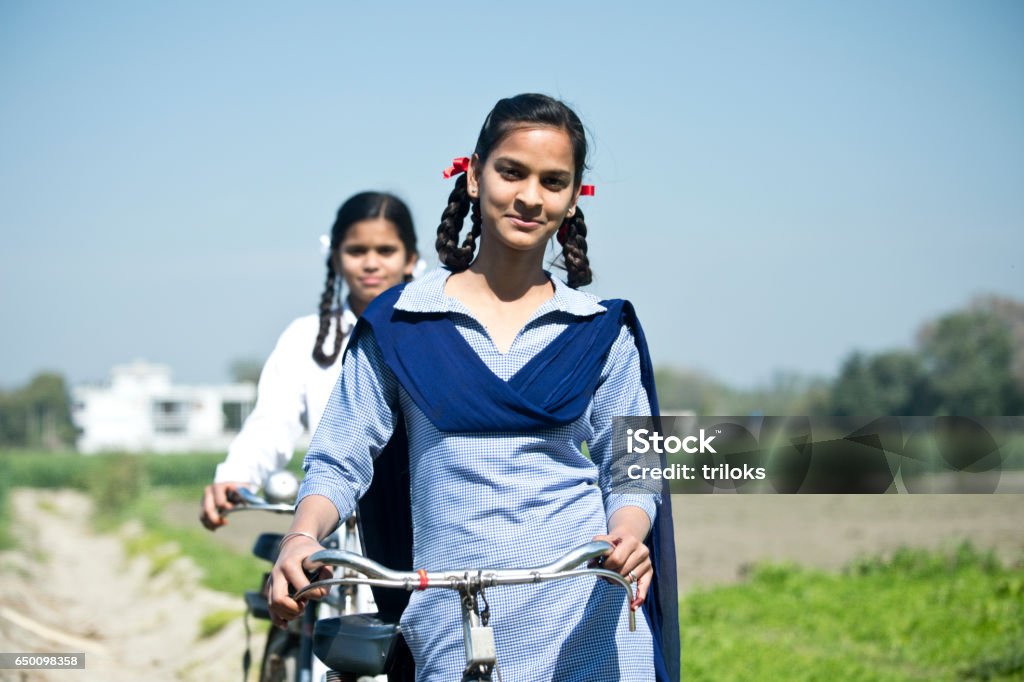 Indian school girls with bicycle Portrait of Indian school girls in uniform walking with bicycle on field Girls Stock Photo