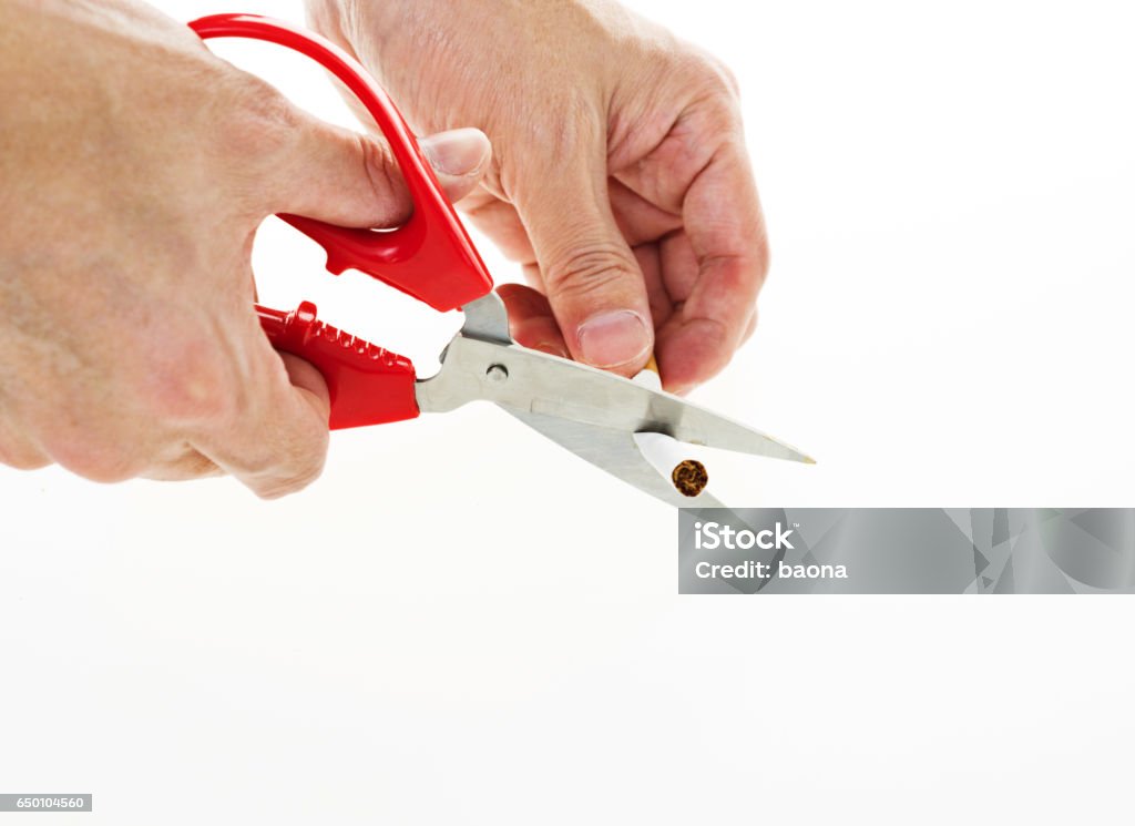 scissors cut a cigarettes Man hand is cutting a cigarette with scissors against white background. Addiction Stock Photo