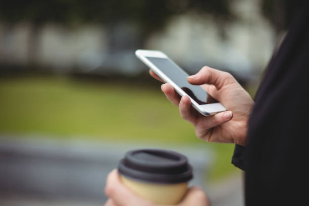 istock Mid section of businesswoman using mobile phone while holding disposable coffee cup 650141922