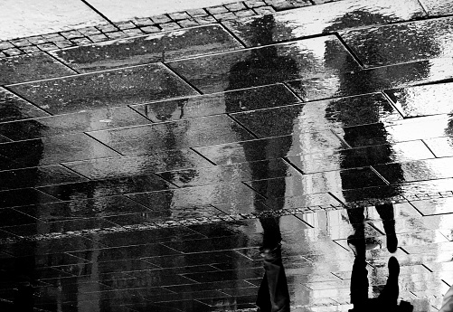 Reflection shadow of a couple walking in the rain in the city pedestrian zone in black and white