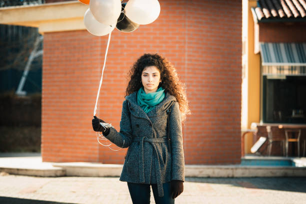 Curly haired and multi raced young girl holding helium balloons