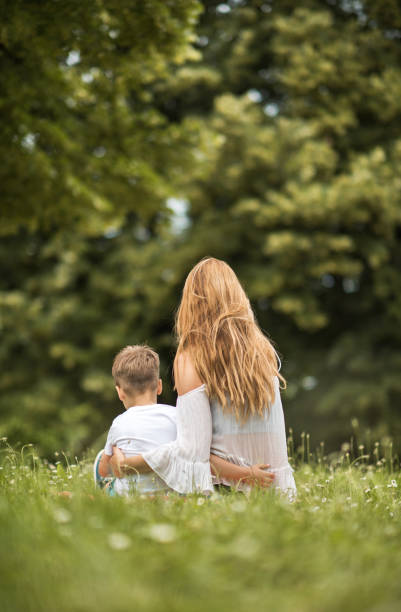 istock Back view of embraced mother and son relaxing in grass. 650169206