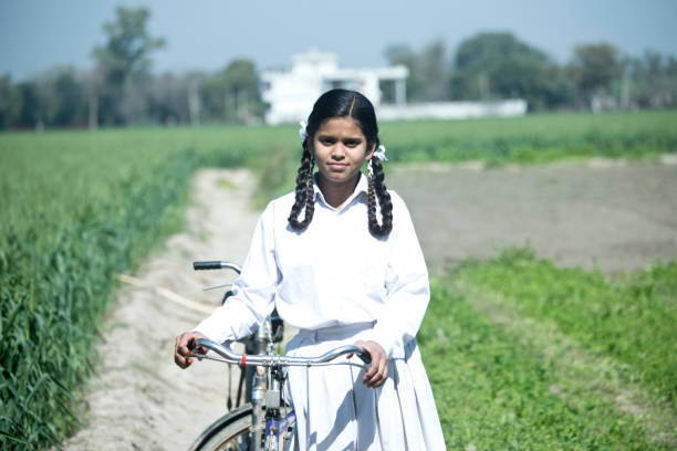 Portrait of Indian school girl in uniform walking with bicycle on field