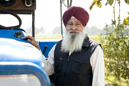 Portrait of old Sikh farmer with tractor on agricultural field