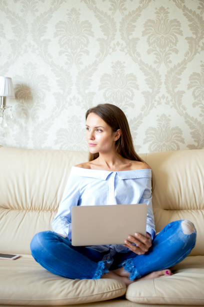 istock Pensive young woman sitting with laptop on sofa 650218624