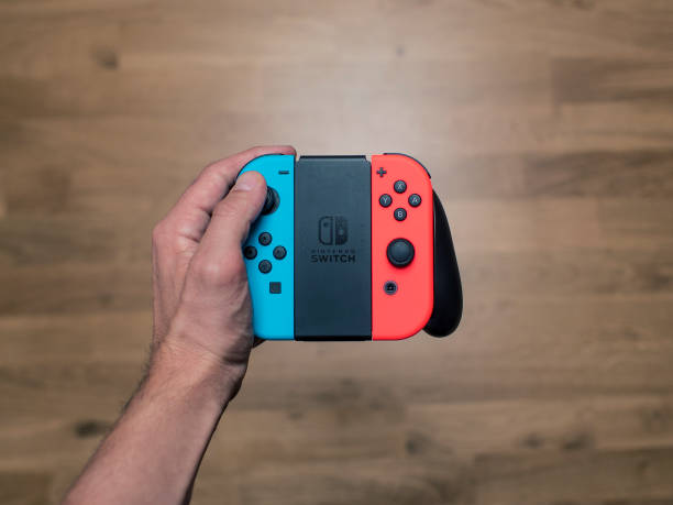 Nintendo Switch neon Game Controller Gothenburg, Sweden - March 6, 2017: A shot from above of a young man's hand holding a Nintendo Switch game controller, a neon coloured remote controller for the Nintendo Switch video game system developed and released by Nintendo Co., Ltd. in 2017. Shot on a wooden background in a home environment. brand name games console stock pictures, royalty-free photos & images