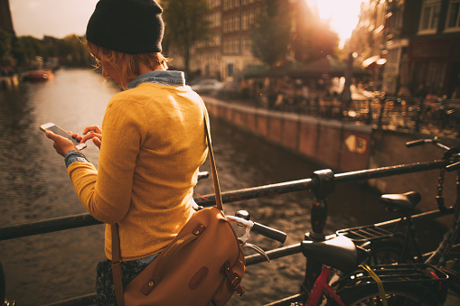 Photo of a young woman using her mobile phone for finishing her work, while walking the sunny streets of Amsterdam