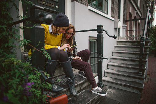 Couple of friends sitting on a doorstep, and using mobile phone for social networking