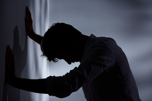 Man leaning with hands against wall, dark room