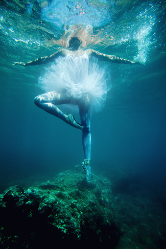 Underwater shot of ballerina in white tutu making the ballet pose with arms outstretched under the sea.