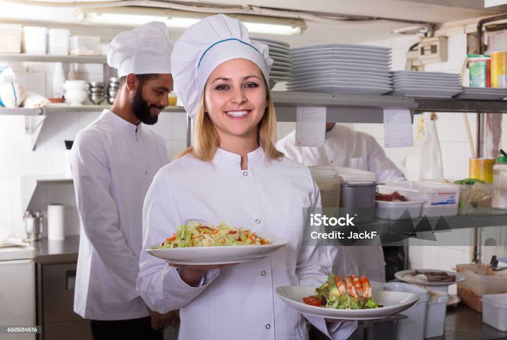 chef and his assistants preparing meal Smiling chef and his assistants preparing meal in kitchen indoors Cafe Stock Photo