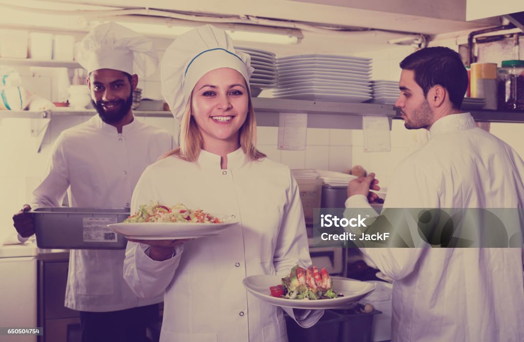chef and his assistants preparing meal Smiling chef and his assistants preparing meal in tavern indoors Crew Stock Photo