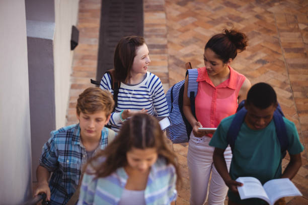 istock Students holding books and digital tablet walking through school campus 650580286