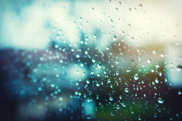 Full frame selective focus on raindrop water on clean window, with houses, trees and sunlight emerging out of focus in background, blurred by lens focus. Background with copy space ready for design.